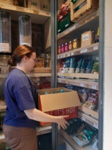 Alina füllt aus einem Karton Ware im Laden nach
